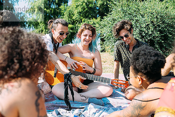 Gruppe von Freunden entspannt sich  spielt Gitarre beim Picknick im Park