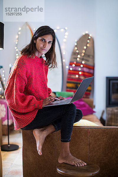 Junge Frau in rotem Pullover auf Wohnzimmersofa mit Laptop  Portrait