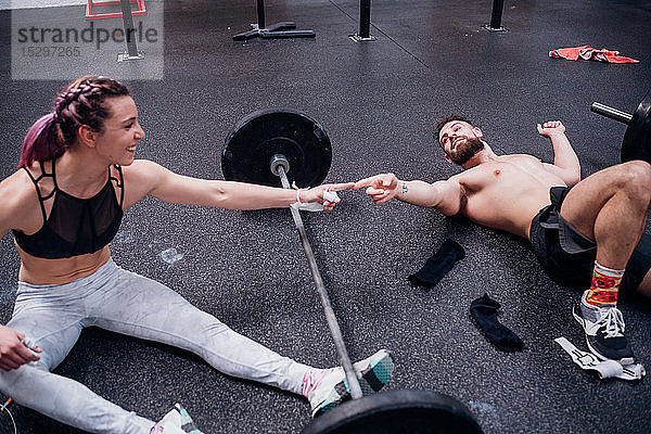 Junge Frau und Mann trainieren zusammen und berühren sich im Fitnessstudio mit den Fingern über der Hantel