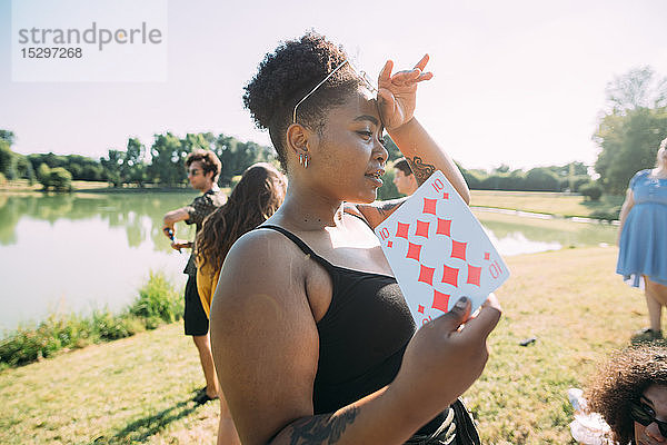Junge Frau kühlt sich mit Spielkarte im Park ab