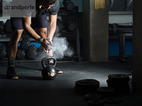 Mann pudert sich die Hände vor dem Heben der Kettlebell im Fitnessstudio