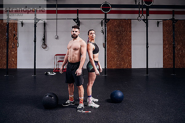 Junge Frau und Mann trainieren zusammen  Rücken an Rücken Portrait im Fitnessstudio