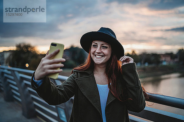 Junge Frau mit langen roten Haaren auf dem Steg beim Smartphone-Selfie in der Abenddämmerung  Florenz  Toskana  Italien