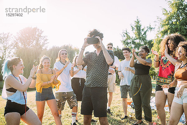 Gruppe von Freunden beobachtet Mann  der im Park in ein VR-Headset schaut