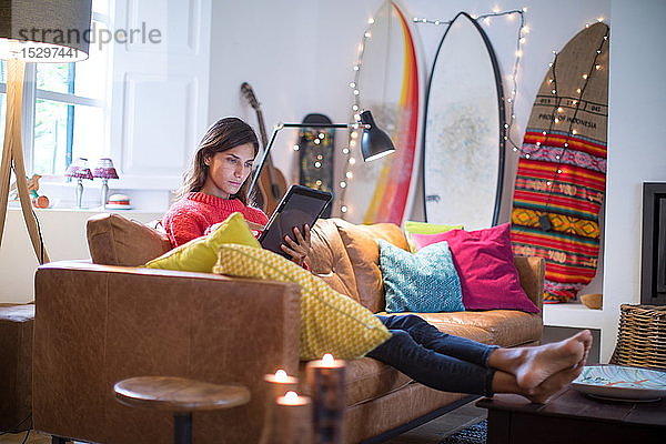 Junge Frau entspannt sich auf Wohnzimmer-Sofa und schaut auf digitales Tablet