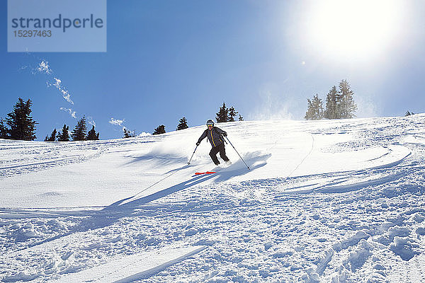 Reifer Mann fährt mit Skiern den sonnenbeschienenen schneebedeckten Berg hinunter  Steiermark  Tirol  Österreich
