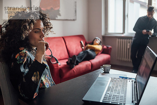 Frau benutzt Laptop  Freunde entspannen sich im Hintergrund im Home-Office