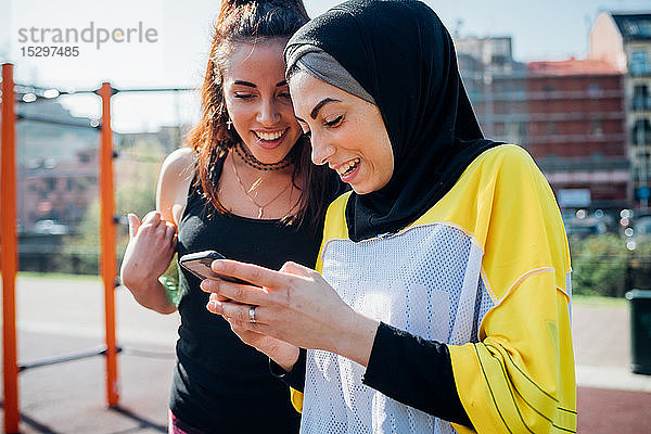 Calisthenics-Kurs im Outdoor-Fitnessstudio  zwei junge Frauen schauen auf ein Smartphone