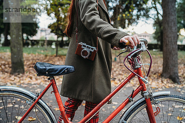 Junge Frau schiebt Fahrrad im Herbstpark mit gesenktem Hals