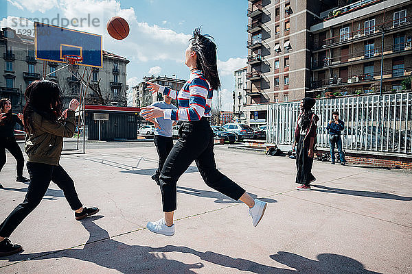 Junge weibliche und männliche erwachsene Freunde spielen Basketball auf dem städtischen Basketballfeld