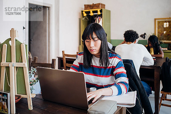 Junge Geschäftsfrau arbeitet ferngesteuert am Laptop am Cafétisch