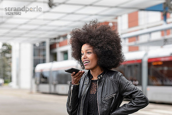 Junge Frau mit Afro-Haaren am Stadtbahnhof  spricht mit Smartphone