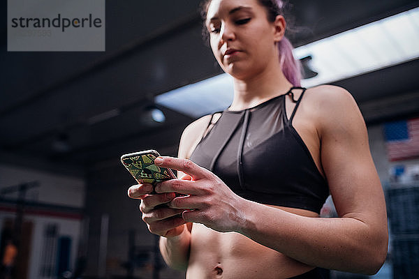 Junge Frau beim Training  Blick auf das Smartphone im Fitnessstudio  Blick aus niedrigem Winkel