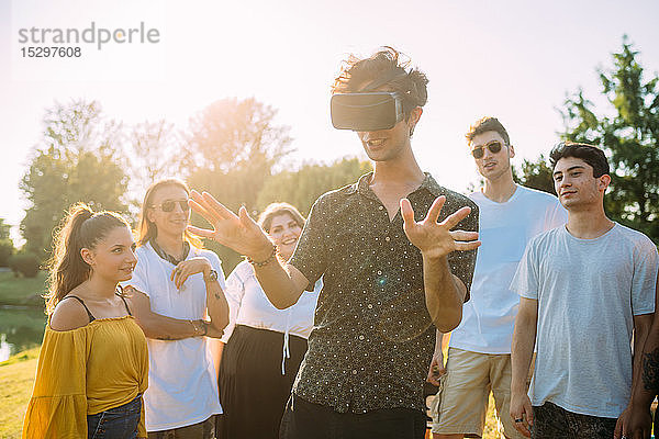 Gruppe von Freunden beobachtet Mann  der im Park in ein VR-Headset schaut