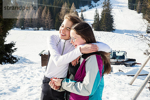 Zwei jugendliche Skifahrerinnen umarmen sich in schneebedeckter Landschaft  Rückansicht  Tirol  Steiermark  Österreich