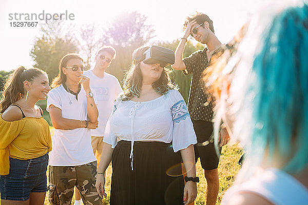 Gruppe von Freunden beobachtet Frau  die im Park in ein VR-Headset schaut