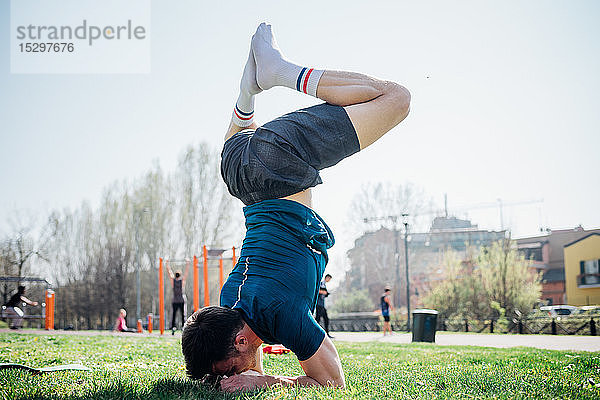 Gymnastik im Freien  junger Mann kopfüber in Yogastellung auf Rasen