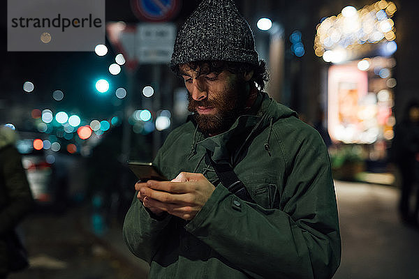 Bärtiger junger Mann benutzt Smartphone auf der Straße