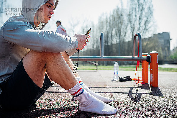 Calisthenics-Kurs im Fitnessstudio im Freien  junger Mann setzt sich hin und schaut auf das Smartphone