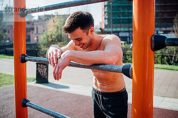 Gymnastik im Fitnessstudio im Freien  junger Mann mit nackter Brust  der sich erschöpft auf Übungsgeräte stützt