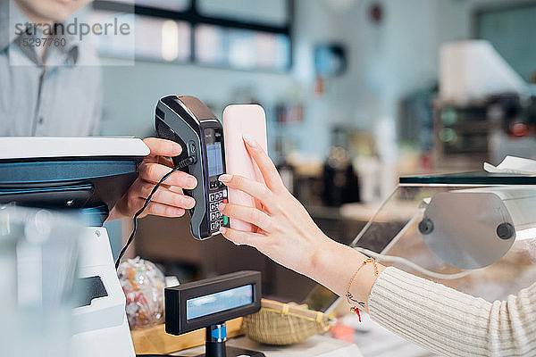 Junge Geschäftsfrau beim Bezahlen per Smartphone an der Cafe-Theke  beschnitten