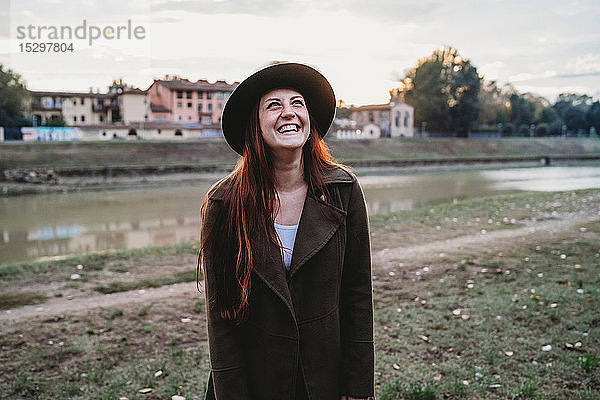 Junge Frau mit langen roten Haaren lacht am Flussufer  Florenz  Toskana  Italien