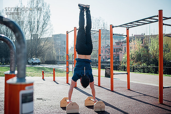 Gymnastik im Fitnessstudio im Freien  junger Mann beim Handstand auf Übungsgeräten  Rückansicht
