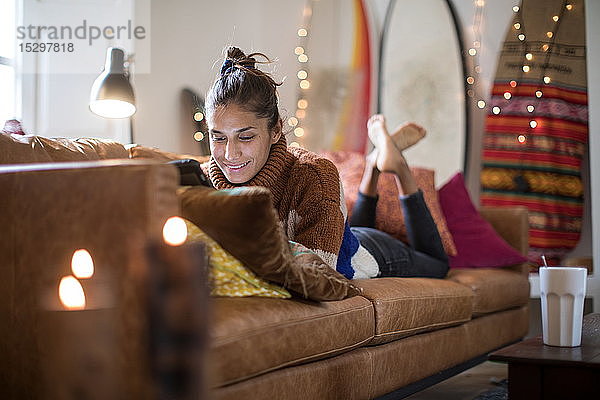 Junge Frau liegt auf Wohnzimmer-Sofa und schaut auf Laptop