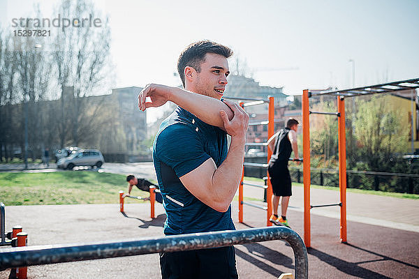 Gymnastik im Fitnessstudio im Freien  junger Mann beim Armstrecken