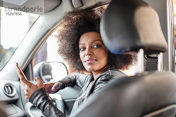 Junge Frau mit Afro-Haaren im Beifahrersitz eines Autos  die ein Smartphone hält  Porträt