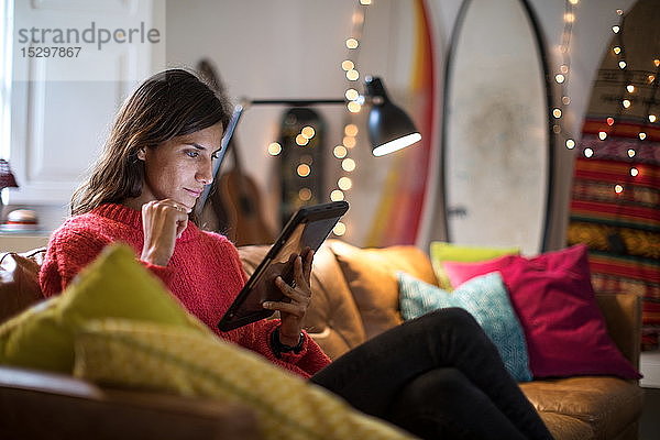 Junge Frau entspannt sich auf Wohnzimmer-Sofa und schaut auf digitales Tablet