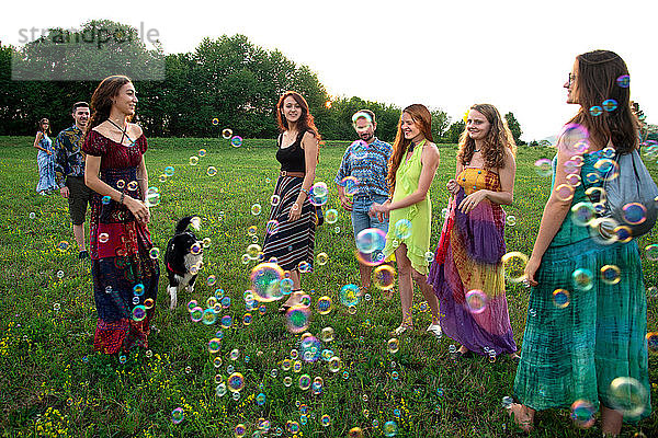 Große Gruppe glücklicher junger Erwachsener steht mit schwebenden Blasen im Feld