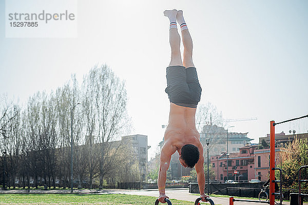 Gymnastik im Freien  junger Mann beim Handstand an Fitnessgeräten  Rückansicht