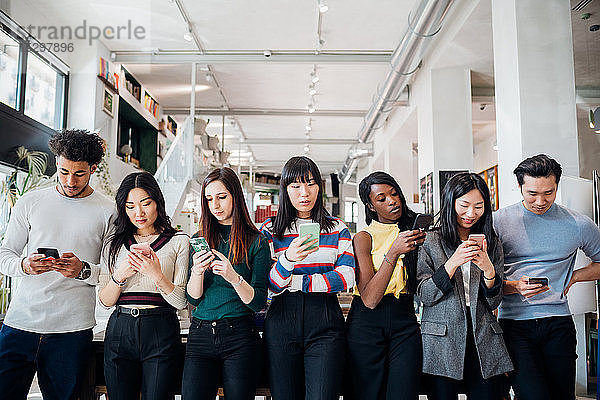 Gruppe von jungen Geschäftsfrauen und -männern in einer Reihe  die sich Smartphones anschauen
