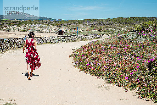 Junge Frau geht am Strand an Blumen vorbei  Alghero  Sardinien  Italien