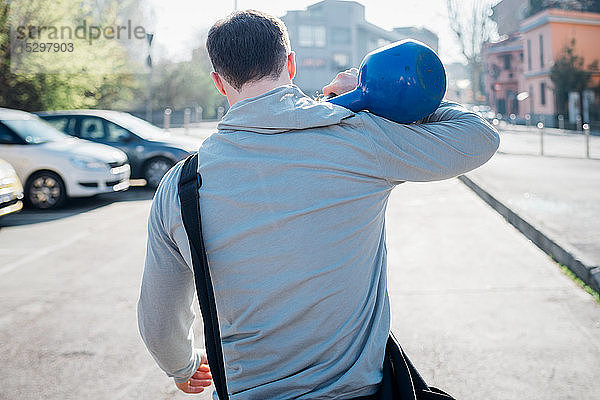 Calisthenics im Park  junger Mann mit einer Kettlebell über der Schulter  Rückansicht
