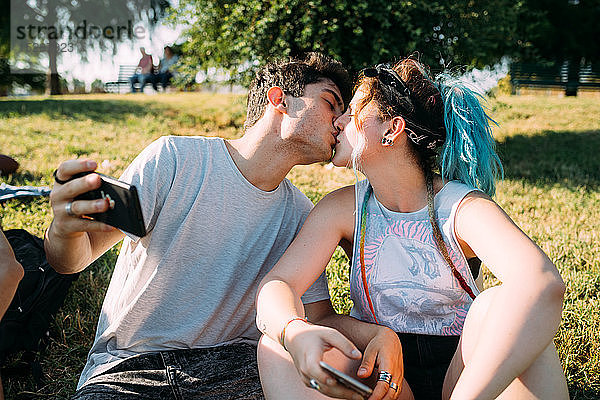 Küssen zu zweit  Smartphone im Park benutzen