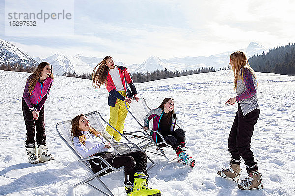 Fünf jugendliche Skifahrerinnen im Stehen und in Liegestühlen in verschneiter Landschaft  Tirol  Steiermark  Österreich