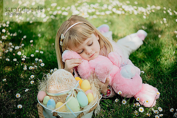 Süßes Mädchen im Gras liegend mit Spielzeugkaninchen und Ostereierkorb