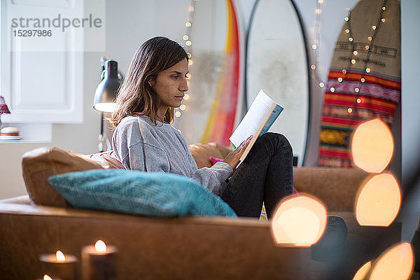 Junge Frau sitzt auf einem Wohnzimmersofa und liest ein Buch