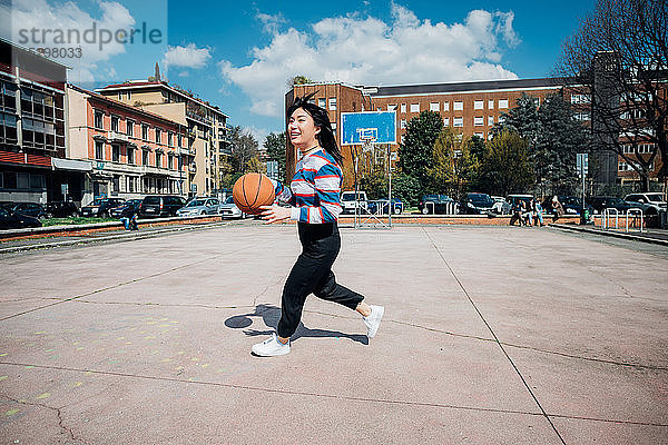 Junge Frau spielt Basketball auf städtischem Basketballfeld