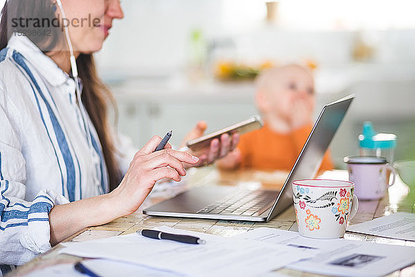 Ein Teil der berufstätigen Mutter nutzt Technologien  während die Tochter im Hintergrund am Esstisch sitzt