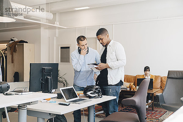 Männliche IT-Fachleute diskutieren über ein digitales Tablet  während sie im Kreativbüro an der Wand stehen