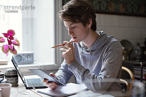 Ernstzunehmender Teenager benutzt digitales Tablett beim Erledigen von Hausaufgaben auf dem Tisch