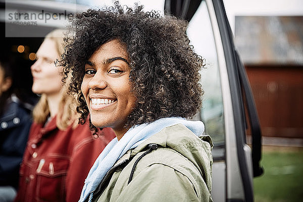 Porträt einer lächelnden jungen Frau mit lockigem Haar  die mit einem Freund im Auto steht