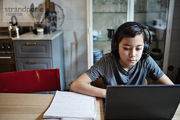 Junge trägt Kopfhörer  während er den Laptop bei den Hausaufgaben zu Hause benutzt