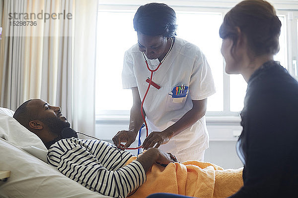 Ärztin untersucht Patientin durch Besucher bei Routinekontrolle auf der Krankenhausstation