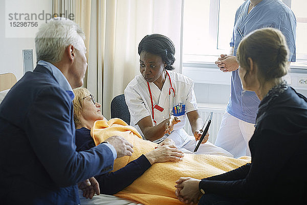 Arzt und Krankenschwester erklären der reifen Patientin und ihren Freunden auf der Krankenhausstation