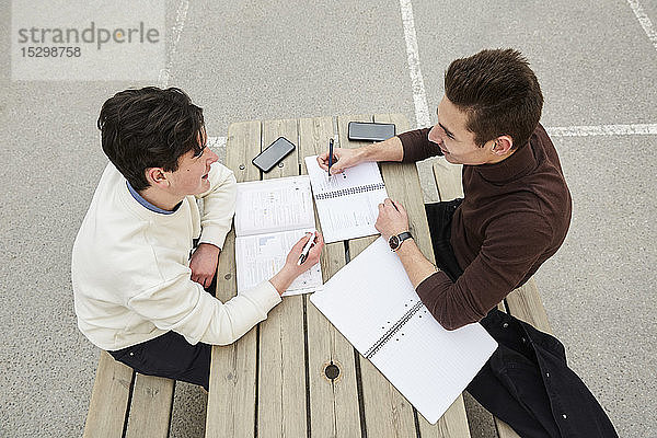 Hochwinkelaufnahme von lächelnden Teenager-Jungen beim Lernen am Tisch auf dem Schulhof