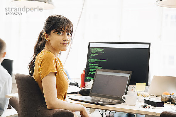 Porträt einer Programmiererin  die im Büro am Schreibtisch sitzt und einen Laptop benutzt
